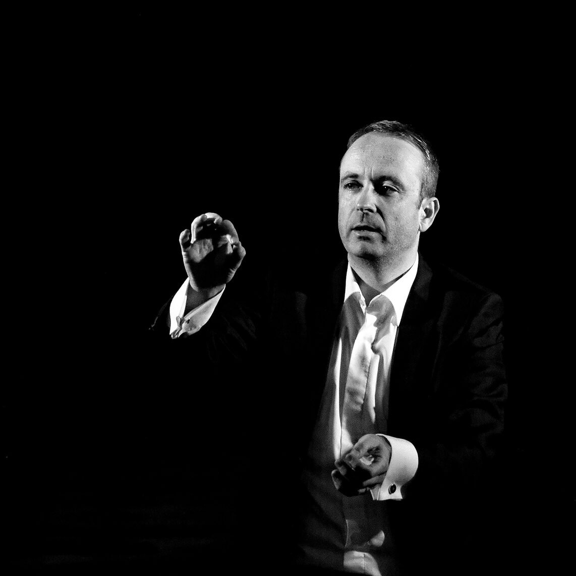 Photo en noir et blanc de Laurent Ottaviani en train de diriger pendant un concert. Il porte une veste de costume noire sur une chemise blanche.